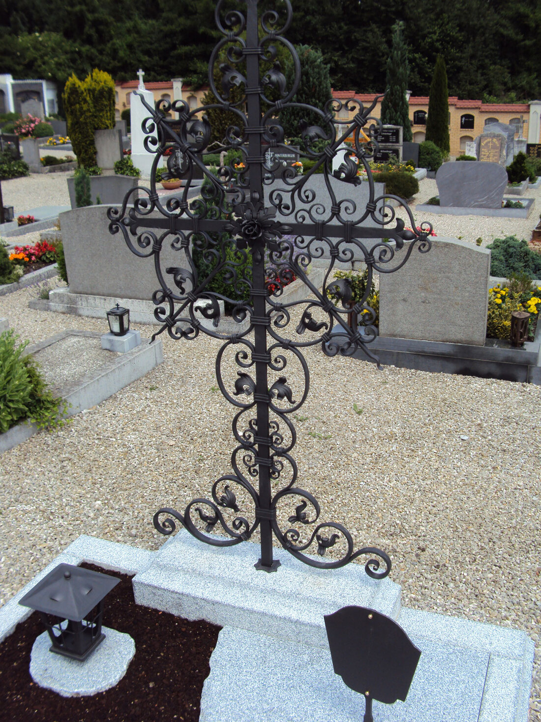 Grab am Friedhof mit einem schwarzen, geschmiedeten Kreuz mit verschnörkelten Elementen