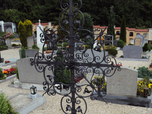 Grab am Friedhof mit einem schwarzen, geschmiedeten Kreuz mit verschnörkelten Elementen
