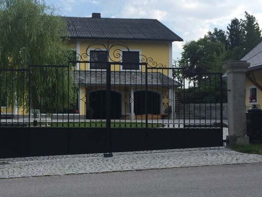 Außenansicht eines geschmiedeten Einfahrtstores vor einem gelben Haus