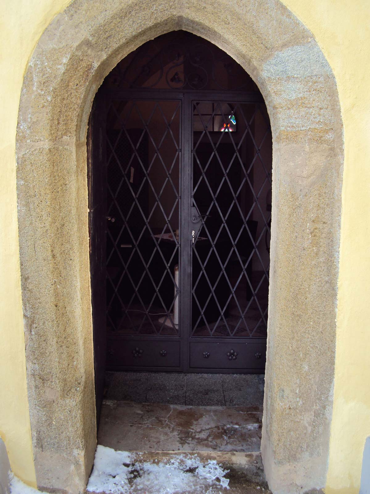 Geschmiedete Kirchentüre 2-flügelige Eingangstüre bei gelber Kirche. Stahltüre geschmiedet, gelocht und Stäbe durchgesteckt.